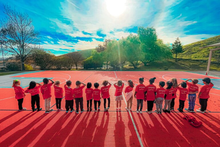 children standing in a line on side of an outdoor court